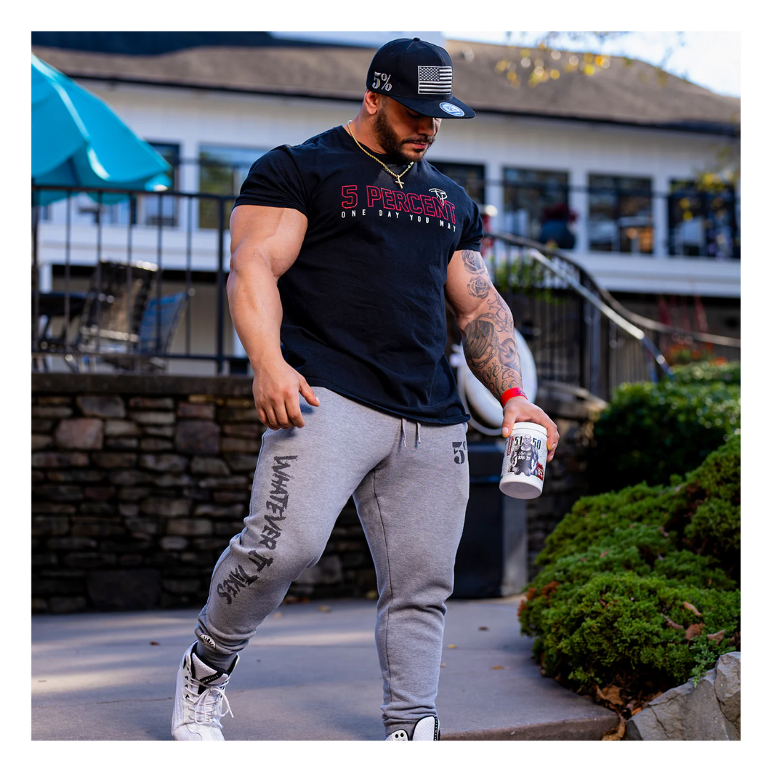 Man in black t-shirt and gray sweatpants holding a cup outdoors