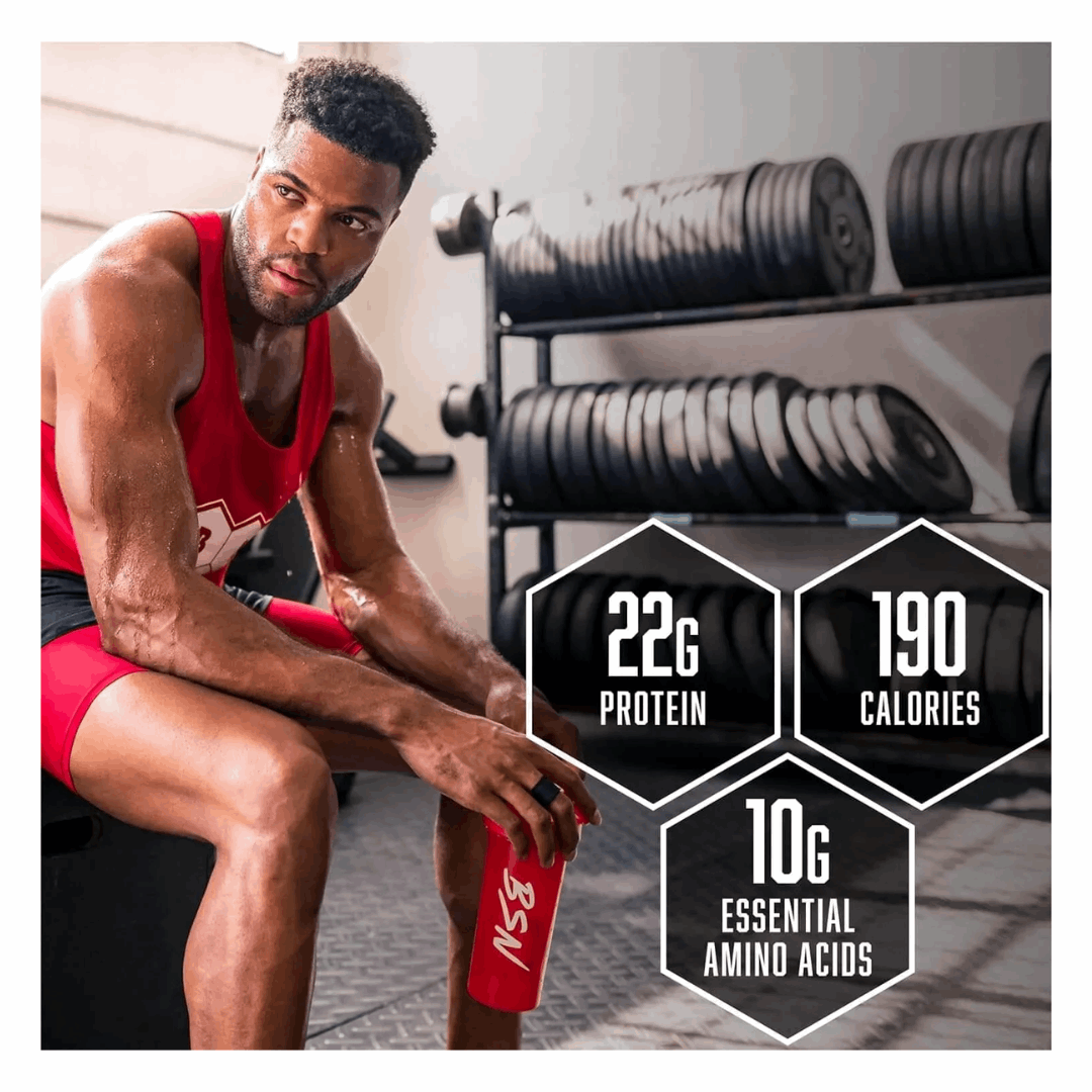 Man in red tank top sitting in a gym holding a protein shaker with nutritional information displayed.