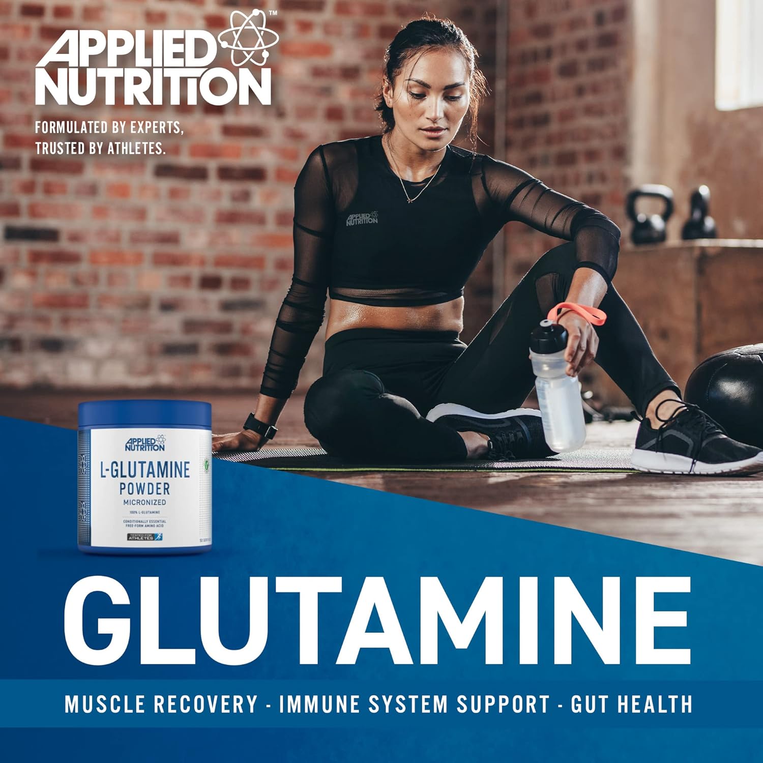Woman sitting on a yoga mat with Applied Nutrition glutamine powder container in foreground, brick wall background